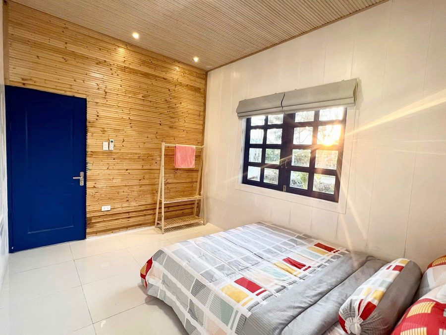 Phòng ngủ homestay ốp gỗ, chăn ấm, cửa sổ nhìn ra vườn